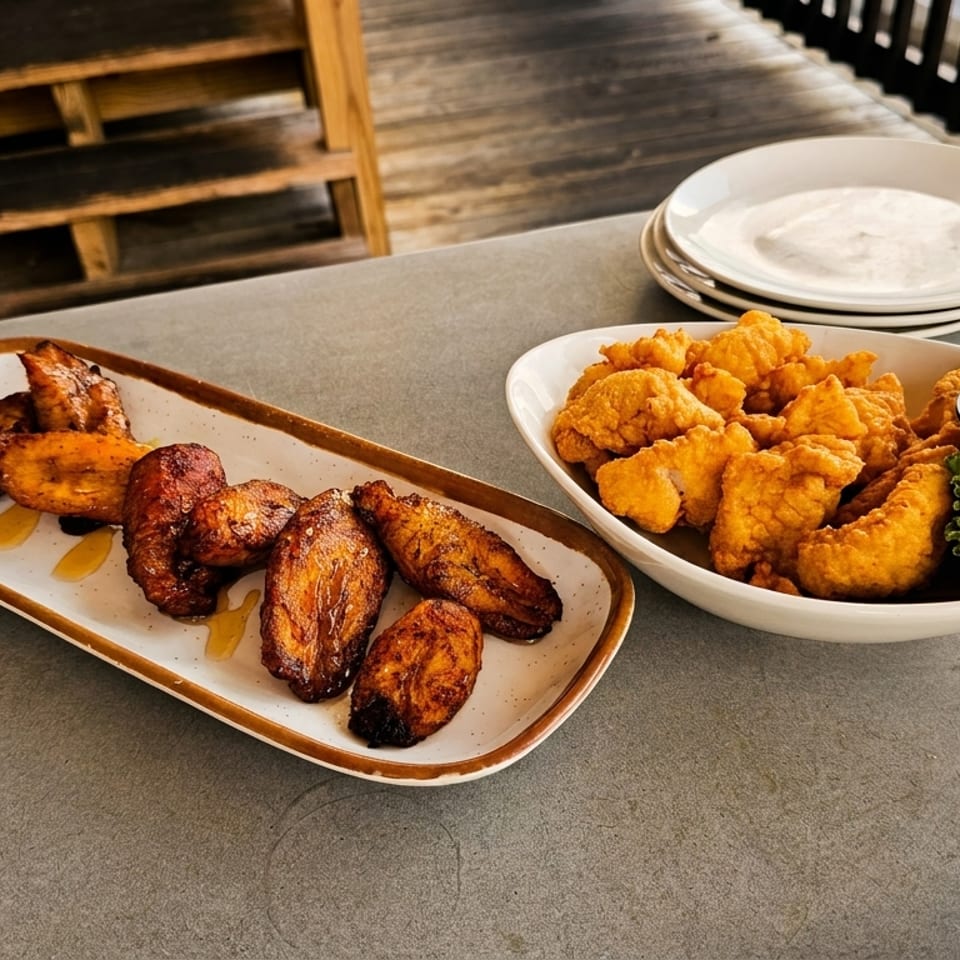 Plates of fried chicken wings and fried shrimp with dipping sauce on an outdoor patio table.