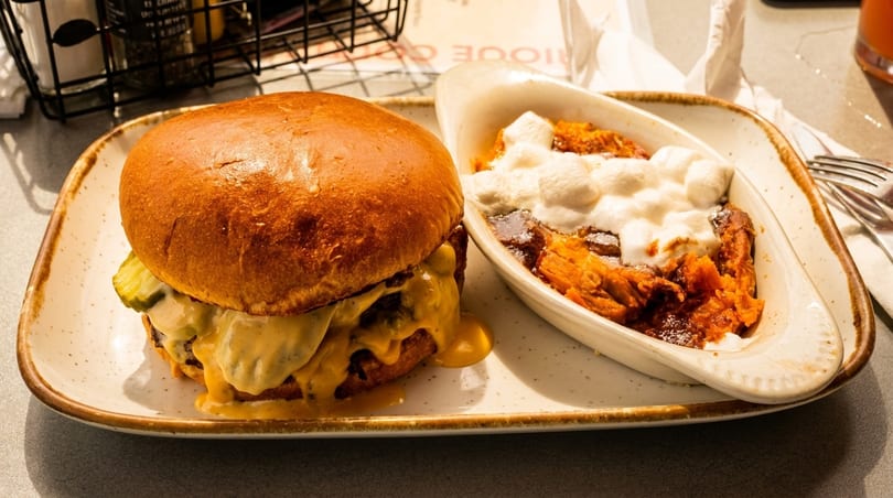 Cheeseburger with pickles and melted cheese, alongside a dish of sweet potato casserole with marshmallows.
